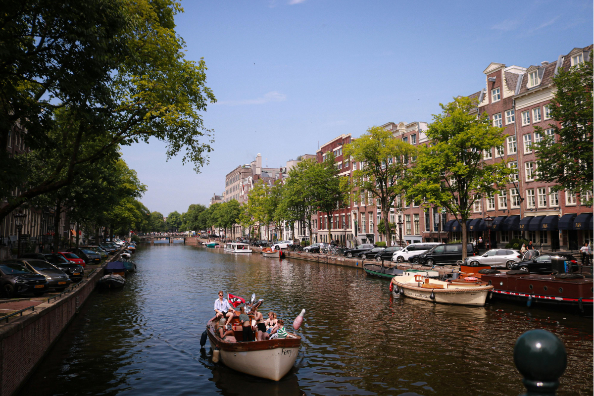 Couple walking beside Amsterdam canal during golden hour with bikes and bridge lights